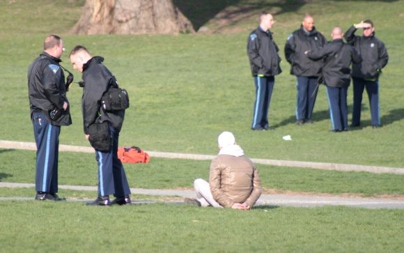 A person who appears to be handcuffed is watched over by Boston Police officers on Boston Common.